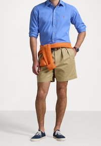 Svetle modrá košile na zapínání, khaki kraťasy, oranžový svetr uvázaný kolem pasu, tmavě modré plátěné boty. Má přiléhavý střih a klasické designové prvky.