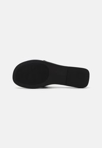 Semelle de chaussure noire avec une texture en caoutchouc lisse et un motif strié pour l'adhérence. Forme légèrement profilée, conçue pour le confort et la stabilité.