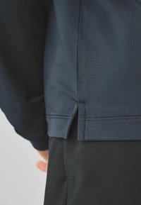 Top de manga larga azul marino con un dobladillo lateral, textura suave y costuras planas, combinado con pantalones negros con textura.