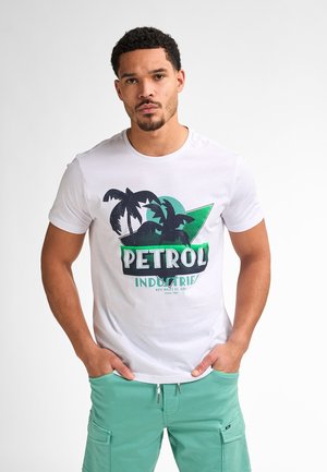 Bílá bavlněná tričko s grafikou palmových stromů a textem "PETROL INDUSTRIES", spárováno se zelenými cargo šortkami. Ležérní střih.