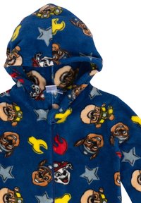 Tuta in pile blu con cappuccio, caratterizzata da personaggi di cani a cartoni animati, stelle e strumenti in colori vivaci. Chiusura con zip frontale e texture morbida.