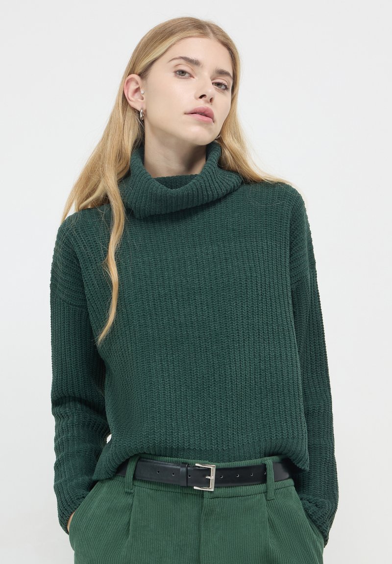 Grüner Strickrollkragenpullover mit strukturiertem Finish, lässiger Schnitt und langen Ärmeln, kombiniert mit hoch taillierten grünen Cordhosen.