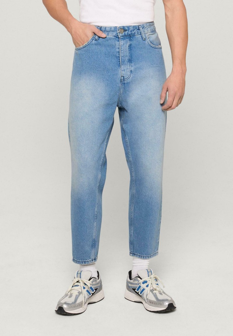 Světle modré denimové džíny s uvolněným střihem, vysokým pasem, bočními kapsami a mírným vyblednutím, spárované se šedými teniskami.