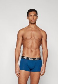 Blue boxer shorts made of soft fabric, featuring a black waistband with white "DIM" branding, snug fit, and classic design.