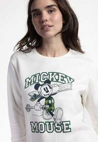 Camicia bianca a maniche lunghe con una grafica colorata di Topolino e dettagli a quadri verdi. Tessuto morbido con colletto a girocollo.