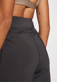 Leggings noirs taille haute en matière extensible. Dotés de coutures plates et d'une texture lisse, conçus pour le confort et la flexibilité.