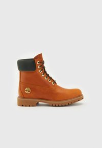 Brązowy skórzany botek za kostkę z czarną, wyściełaną kołnierzem, złotymi oczkami i logo po boku. Posiada solidną podeszwę dla lepszej przyczepności.