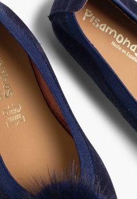 Ballerines en suede bleu marine avec un bout arrondi, dotées d'un accent en pompon de fourrure douce et d'une semelle en cuir, avec des coutures détaillées autour des bords.