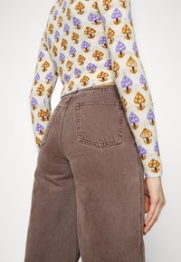 Bruna denimjeans med fem fickor, medelhög midja och en mjuk textur. Tröjan har en krämfärgad bas med bruna och lila svampmönster.