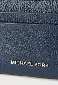 Cuero texturizado azul marino con grano visible, con la marca "MICHAEL KORS" en plata sobre una superficie lisa.