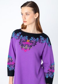 Violet neulepaita mustilla yksityiskohdilla, jossa on monimutkaista kukka-embroiderya vaaleanpunaisella, sinisellä, vihreällä ja keltaisella. Rentoa mallia, leveä pääntie.