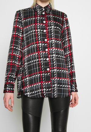 Chemise à manches longues à carreaux noirs, rouges, blancs et gris avec des boutons argentés, portée avec un pantalon en cuir noir texturé.