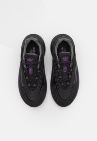 Svarta och lila Adidas-sneakers sedda uppifrån, med snörning knuten och Adidas-logotypen synlig på tungan och innersulan av varje sko.
