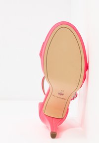 Une chaussure à talons hauts de couleur rose vif se tenant sur son talon, la semelle tournée vers l'avant montrant une semelle beige lisse et une marque de taille 37.