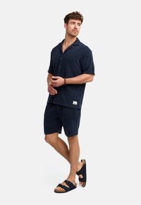 Navy-blaues Frottierhemd mit kurzen Ärmeln und passenden Shorts, die einen lässigen Schnitt haben, kombiniert mit navy-blauen Sandalen mit verstellbaren Riemen.