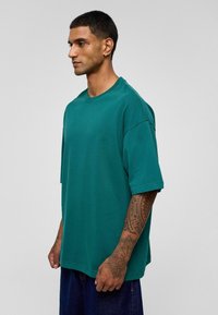Groene katoenen oversized T-shirt met korte mouwen, ronde kraag en naadloos schouderontwerp. Soepele textuur zonder zichtbare patronen.