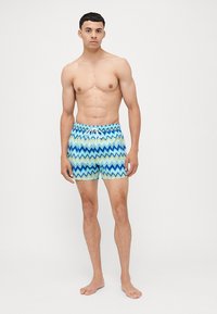 Zig-zag mintás úszónadrág kék és zöld tónusokban. Elasztikus derékpánt, húzózsinórral, könnyű anyagból készült.