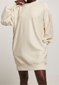 Robe sweat-shirt oversize beige clair avec texture côtelée, col en V et manches longues. Comprend des poches latérales et une coupe décontractée.