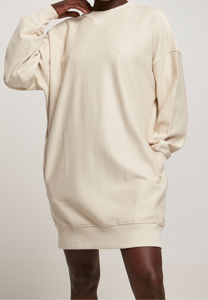 Robe sweat-shirt oversize beige clair avec texture côtelée, col en V et manches longues. Comprend des poches latérales et une coupe décontractée.