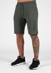 Groene katoenen shorts met een gestructureerd oppervlak, voorzien van een zijzak en een logo-opdruk in zwart. Gepaard met zwarte sportschoenen.
