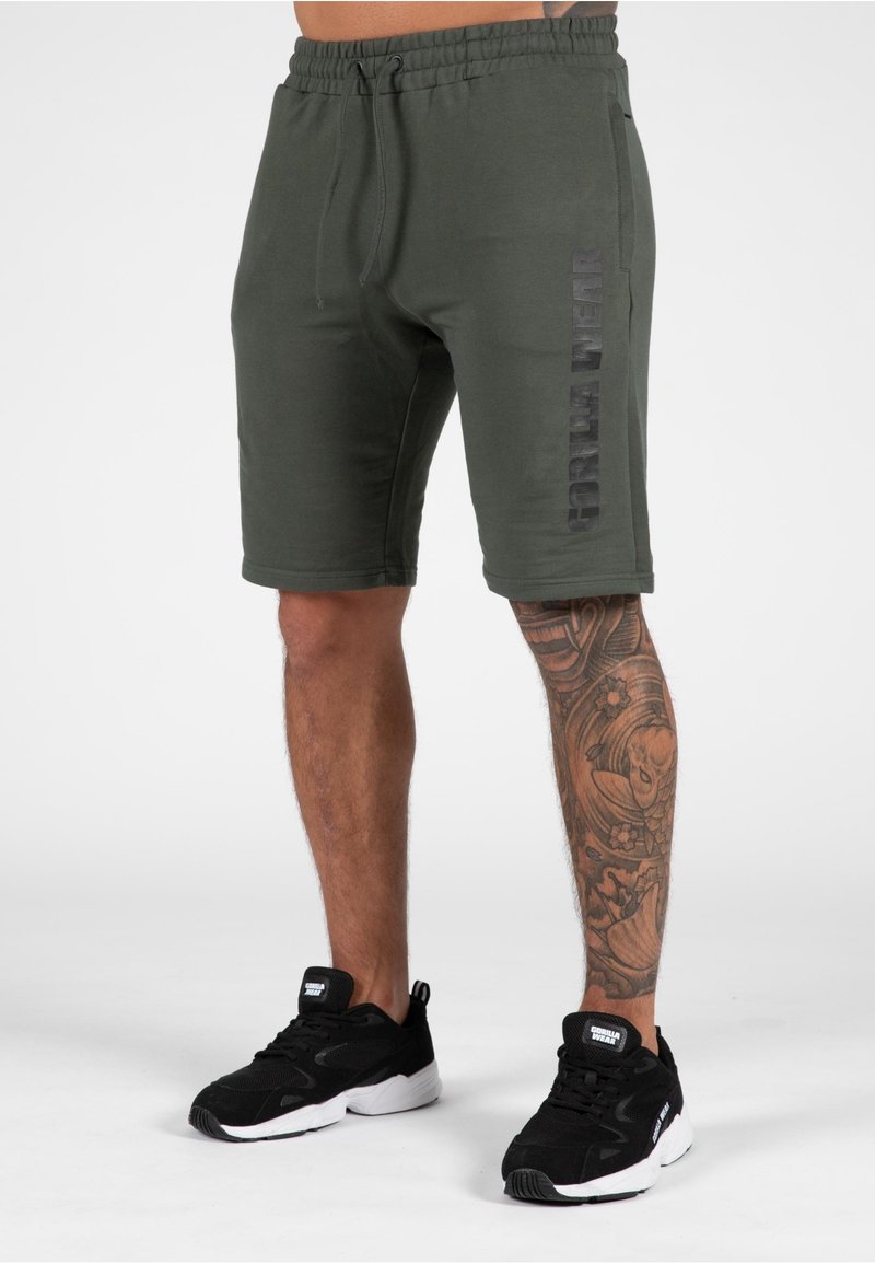 Groene katoenen shorts met een gestructureerd oppervlak, voorzien van een zijzak en een logo-opdruk in zwart. Gepaard met zwarte sportschoenen.