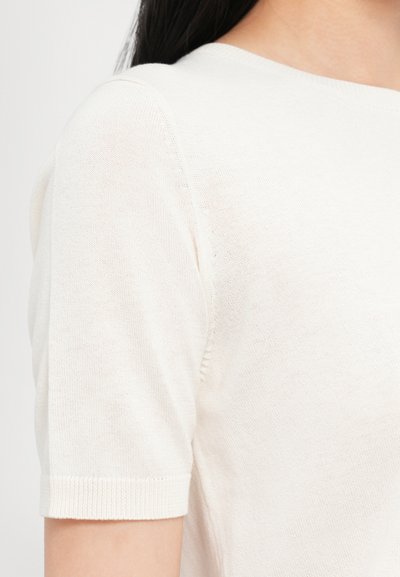 Top lavorato a maglia crema con maniche corte, scollatura rotonda e motivo testurizzato. Il tessuto sembra morbido e leggero.