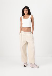 Hvit ribbet crop-top med firkantet halslinje, parret med lyse beige vide bukser med elastisk midje og sidelommer.