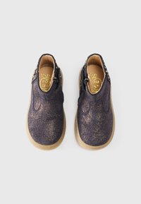 Chaussures marine avec une finition pailletée, bout rond et panneaux latéraux élastiques. Semelles en caoutchouc marron offrant stabilité et adhérence. Logo doré à l'intérieur.