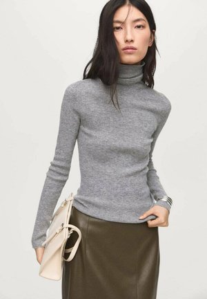 Maglione grigio a coste con colletto a dado e maniche lunghe, abbinato a una gonna verde oliva elegante. Borsa bianca con design minimalista.