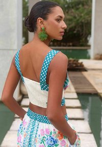Két részes összeállítás, amelyben egy teal színű, mintás crop top széles pántokkal és texturált fehér szegéllyel, valamint zsebes virágmintás szoknya található.