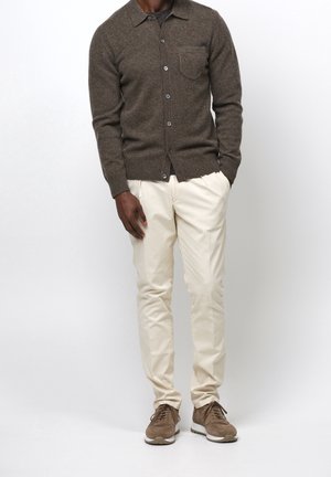Cardigan marrone in lana con colletto, tasca sul petto e chiusura con bottoni; abbinato a pantaloni chinos crema e sneakers in suede marroni.