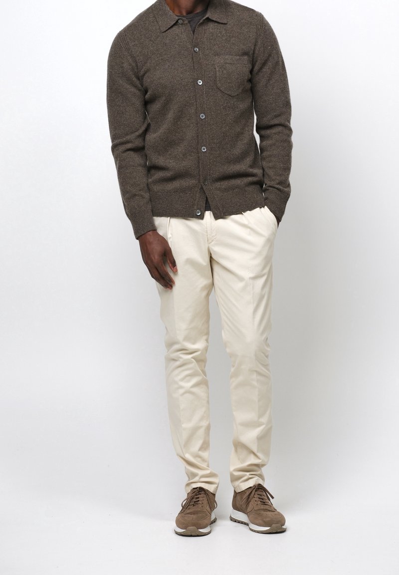 Cardigan en laine marron avec col, une poche poitrine, et fermeture à boutons ; associé à des chino crème et des sneakers en daim marron.