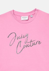 Różowa koszulka Juicy Couture z błyszczącym srebrnym napisem logo i prążkowanym okrągłym dekoltem, rozmiar 9/10 oznaczony wewnątrz kołnierza.