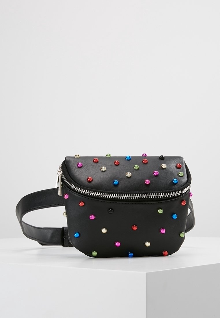 Sac banane en cuir noir décoré de clous ronds multicolores et fermeture éclair argentée, présenté sur une surface blanche.