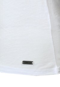 T-shirt bianco a maniche corte con una texture morbida, caratterizzato da un piccolo etichetta di marca nera in tessuto all'orlo. Design semplice senza motivi.