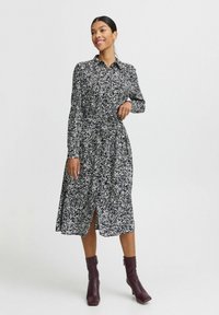 Mustapilkkuinen shirt dress, jossa on pitkät hihat, nappikaulus, terävä vyötärö ja halkio helmaan. Yhdistetty burgundinvärisiin nilkkasaappaisiin.