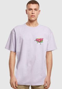 Camiseta de algodón color lila con un gráfico colorido de "WOW" en el lado izquierdo del pecho. El diseño incluye acentos en negrita y un corte relajado.