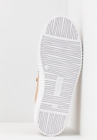 Chaussure brune avec une tige texturée et une semelle en caoutchouc blanche, présentant des rainures horizontales et une marque au niveau de la semelle.