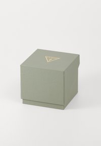 Cutie pătrată, texturată, de culoare verde dezactivată, cu un logo triunghiular auriu în partea de sus. Dispune de o bază solidă și de un sistem de închidere cu clapetă.