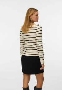Sweter w paski w kremowym i czarnym kolorze, dopasowany fason z długimi rękawami, zestawiony z teksturowaną czarną spódnicą. Gładka struktura dzianiny, minimalne wykończenia.