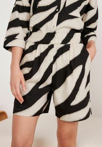 Zwart-witte shorts met een elastische tailleband, met een penseelstrekenontwerp en zijzakken. Lichte stof, casual pasvorm.