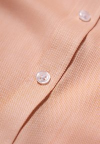 Tessuto di camicia color pesca con un motivo testurizzato. Presenta un bottone trasparente bene in vista vicino a una cucitura.