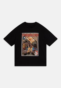T-shirt nera in cotone con una grafica a fumetti colorata che presenta il testo "TIMBERLAND" e una scena naturale, inclusi stivali, montagne e elementi acquatici.
