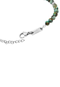 Pulsera de cuentas de piedra turquesa con herrajes de plata, que cuenta con un cierre de langosta y una etiqueta grabada con "BREIL" en una cadena de eslabones metálicos.
