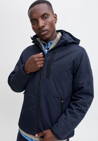 Dunkelblau isolierte Jacke mit Reißverschluss, verstellbarer Kapuze und kontrastierender, strukturierter Fütterung. Verfügt über Fronttaschen und elegante Designelemente.