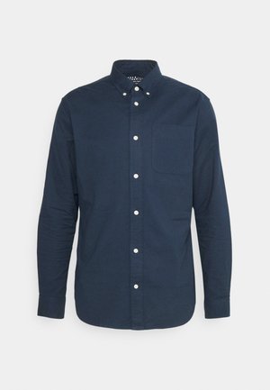 Chemise boutonnée bleu marine en coton, dotée d'une poche poitrine, de manches longues et de boutons blancs le long de la patte de boutonnage.