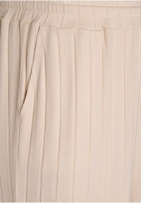 Beige plissierte Hose aus weichem Stoff, mit vertikalen Streifen, einem elastischen Bund und seitlichen Taschen für Funktionalität.