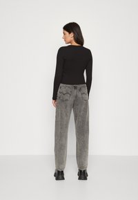 Tricou negru cu mânecă lungă, combinat cu blugi gri, cu talie înaltă și croială largă, având buzunare la spate și detalii de cusătură. Botine negre.