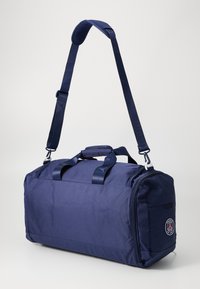 Bolsa de lona azul marino con dos asas, correa de hombro ajustable, cierre de cremallera y emblema de París en el lateral. Textura suave.