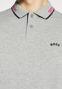 Grå polo skjorta med krage, prydd med två röda ränder och svarta detaljer. Svart "BOSS"-logotyp på vänster bröst. Tillverkad av bomull.